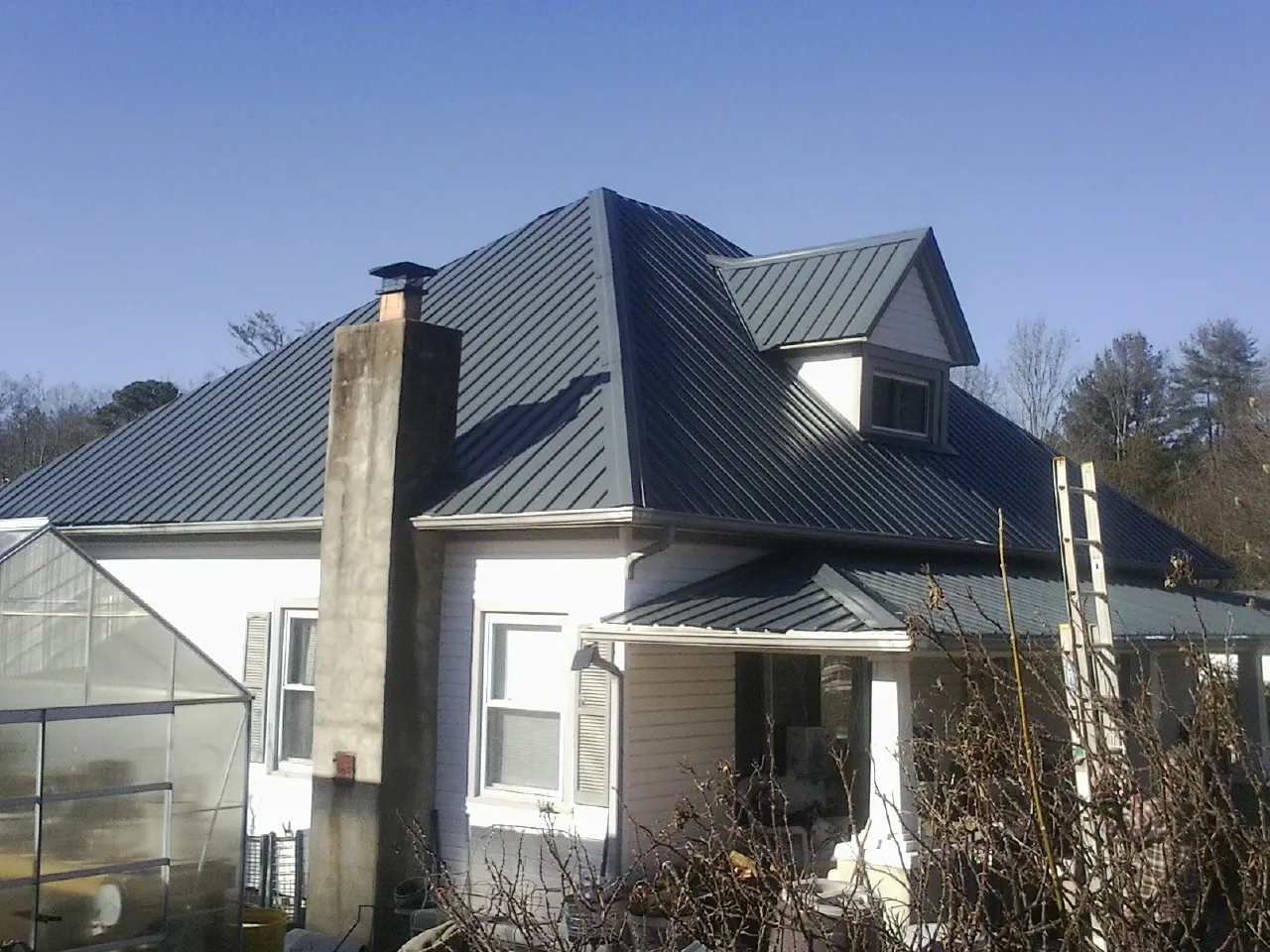Dark blue standing seam metal roof on a white farmhouse with dormer — Slate & Tile Roof Repair by Roofing Brothers in Timberlake