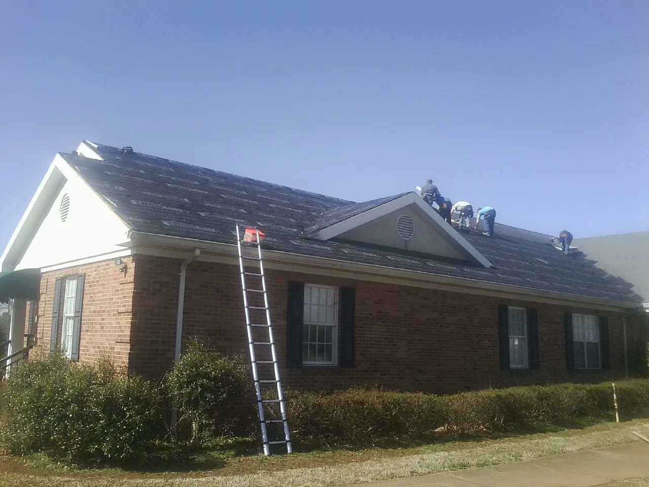Crew tearing shingles off a brick ranch roof with a ladder set — Metal Roof Repair work by our crew in Timberlake