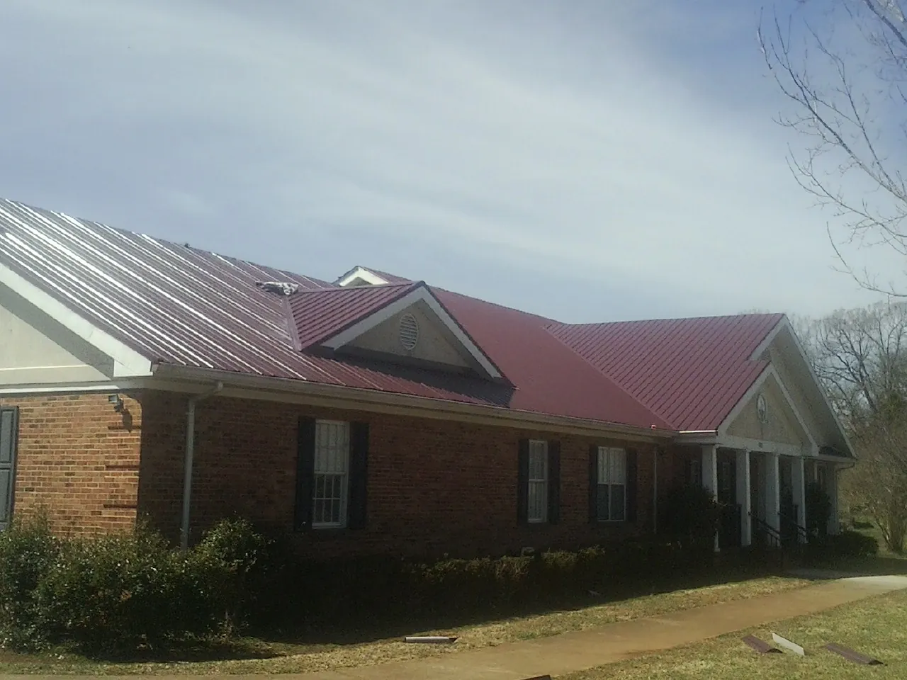 Red metal roof with gabled entries on a long brick building, from a Hail Damage Roof Repair job in Timberlake