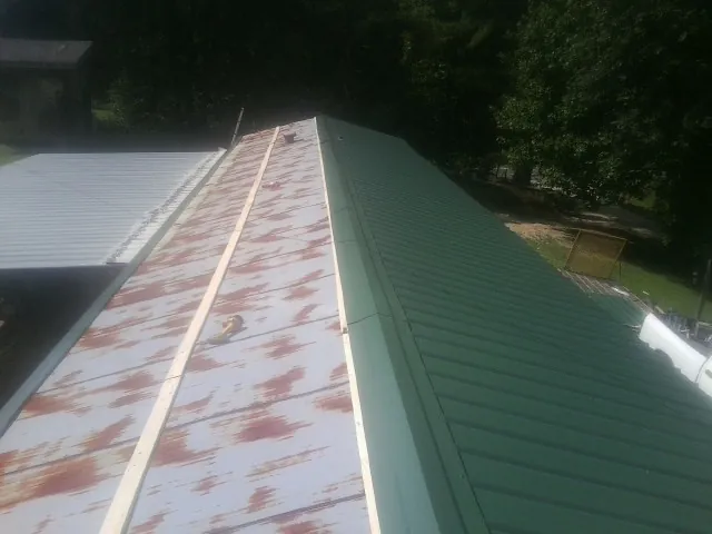 Old rusted panels beside newly installed green metal roofing — Wind Damage Roof Repair by Roofing Brothers in Timberlake