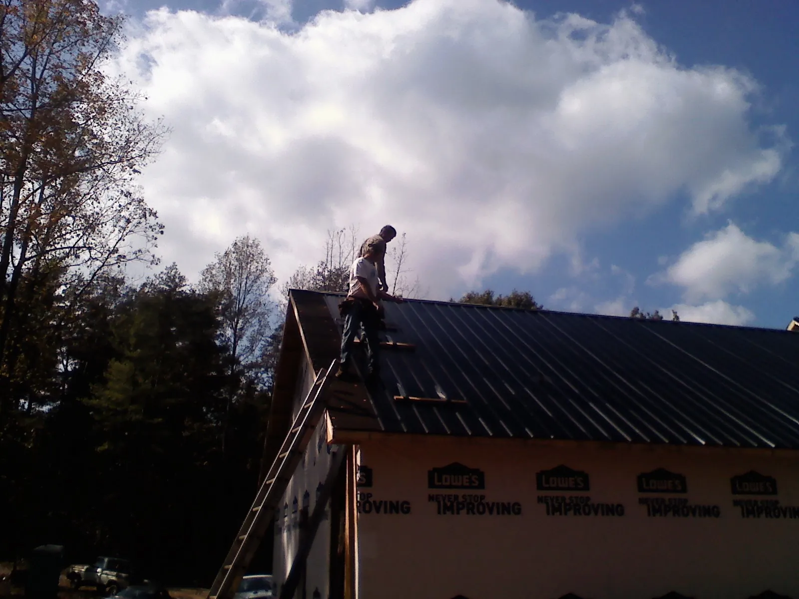 Roofer fastening dark metal panels high against a cloudy sky, from a Roof Inspection job in Timberlake