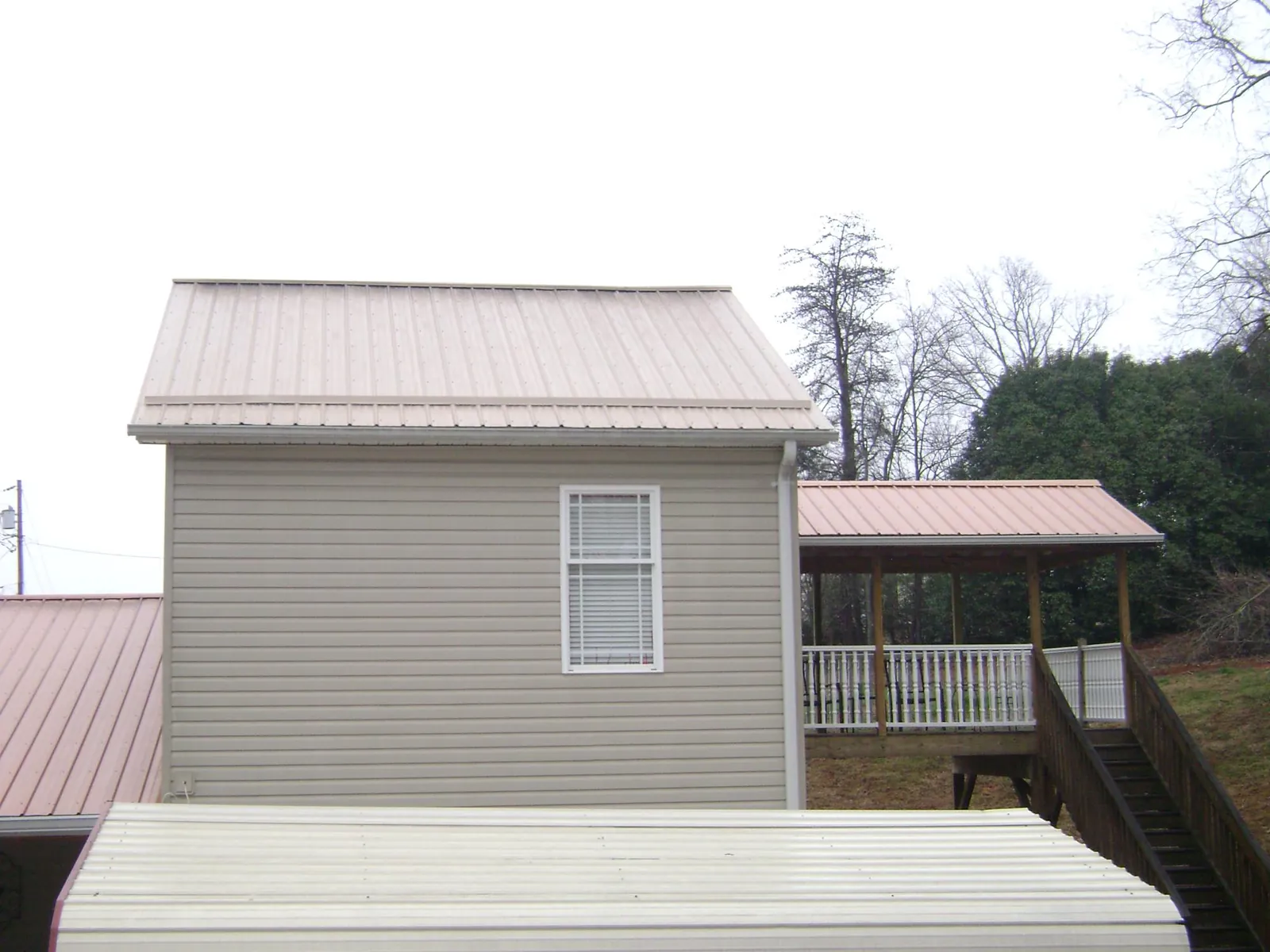 Tan metal roofs on a two story addition and attached porch, from a Roof Replacement job in Timberlake